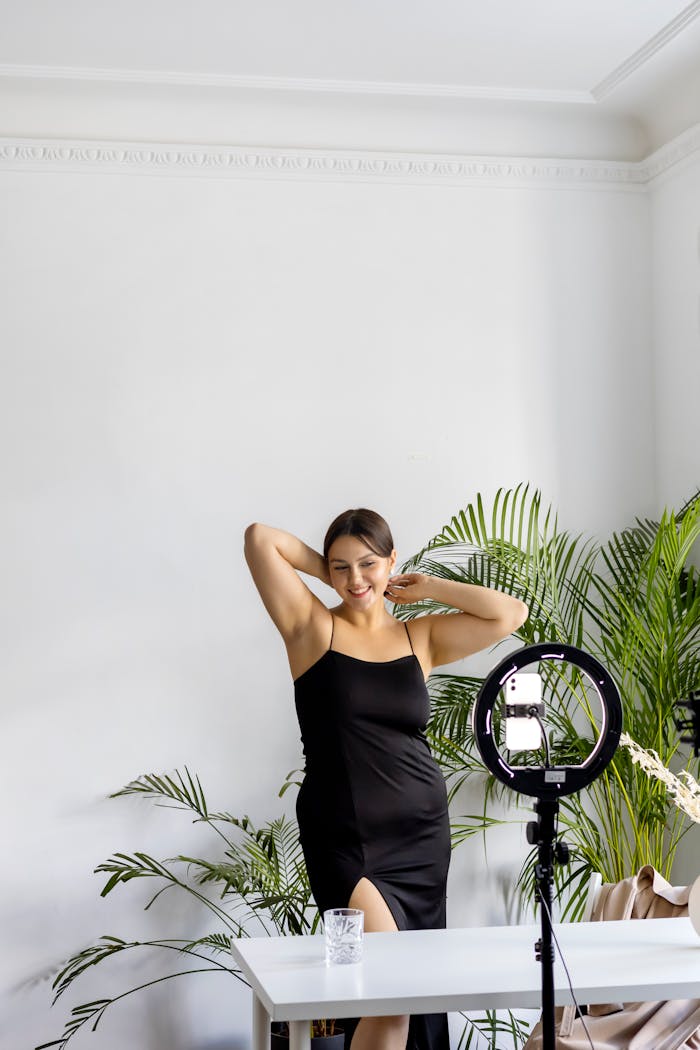 Young woman posing joyfully indoors with a camera setup, embodying modern lifestyle.
